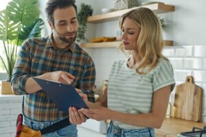 Beautiful young woman signing document while communicating with handyman at the kitchen