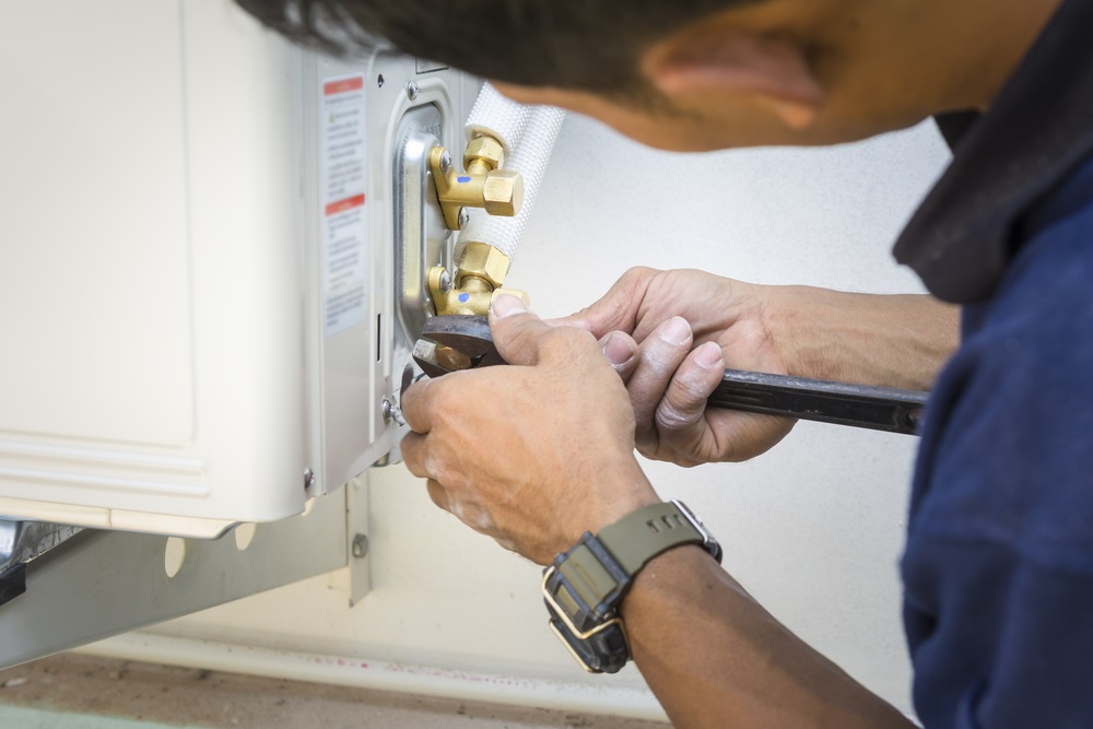 A technician using a wrench to tighten fittings on an air conditioning unit, focusing on mechanical maintenance and repairs