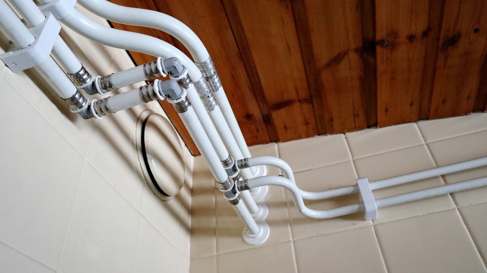 White plumbing pipes connect at angles along a tiled wall beneath a wooden ceiling, showcasing a clean and organized installatio