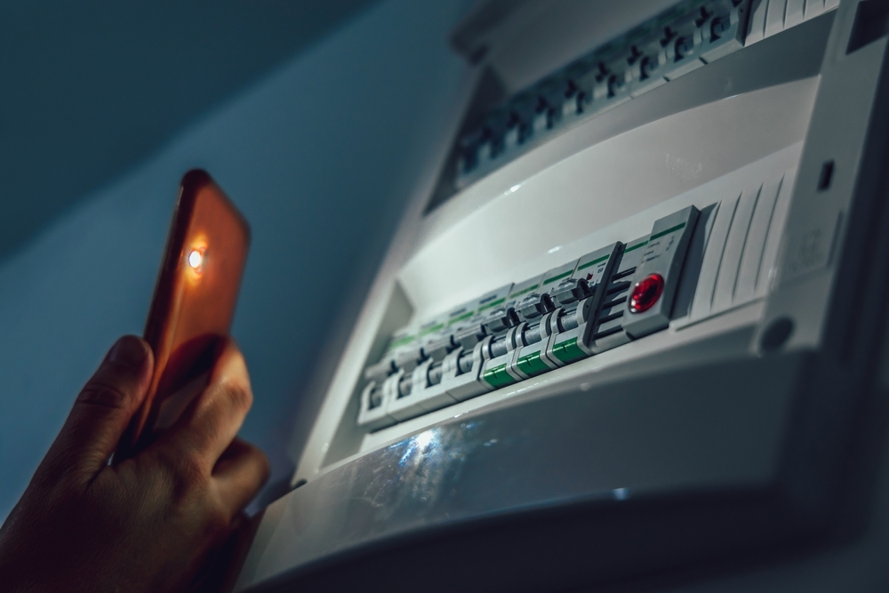 Person inspecting a home electrical breaker panel using a mobile phone flashlight during a power outage