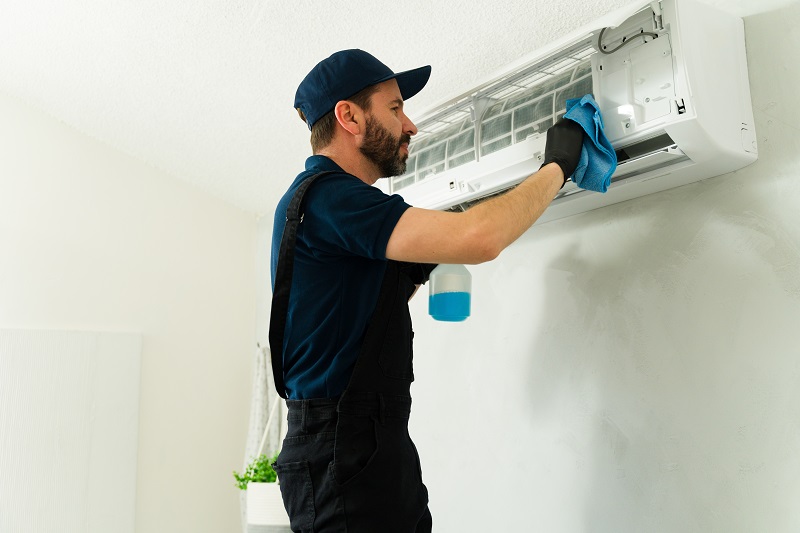 HVAC technician cleaning an air conditioning unit with a cloth and spray bottle