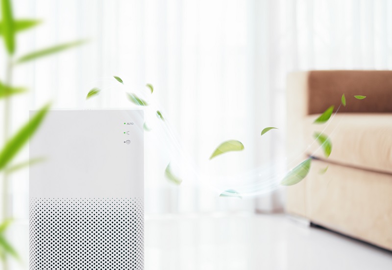 Modern air purifier releasing clean air with floating green leaves in a bright living room
