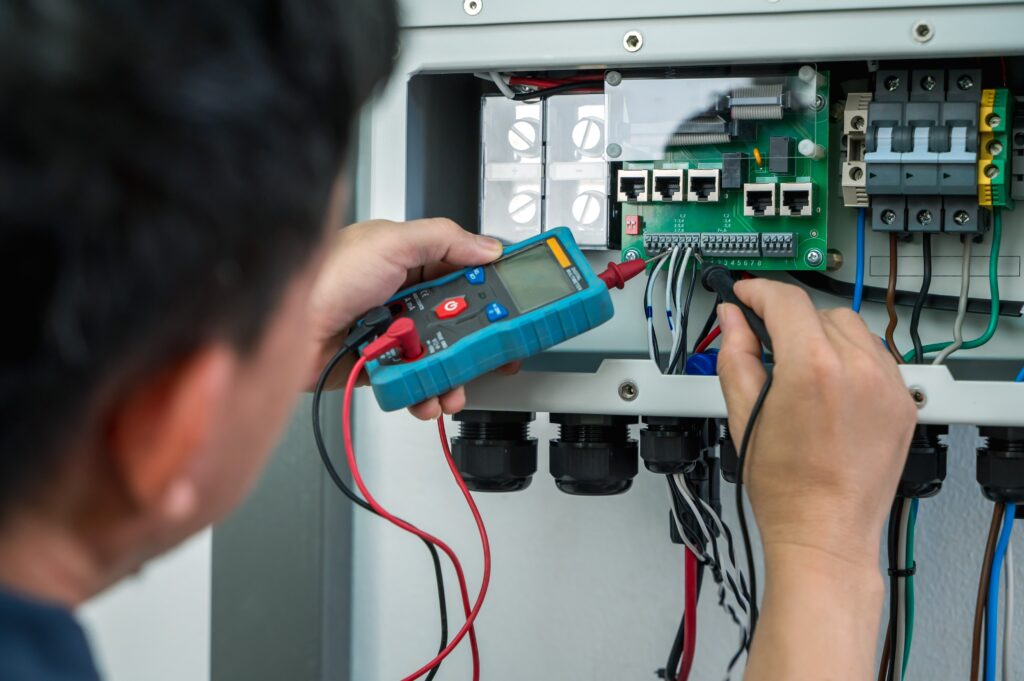 An electrician using a multimeter to test a circuit board, illustrating a technical electrical checkup as part of preventative home maintenance.