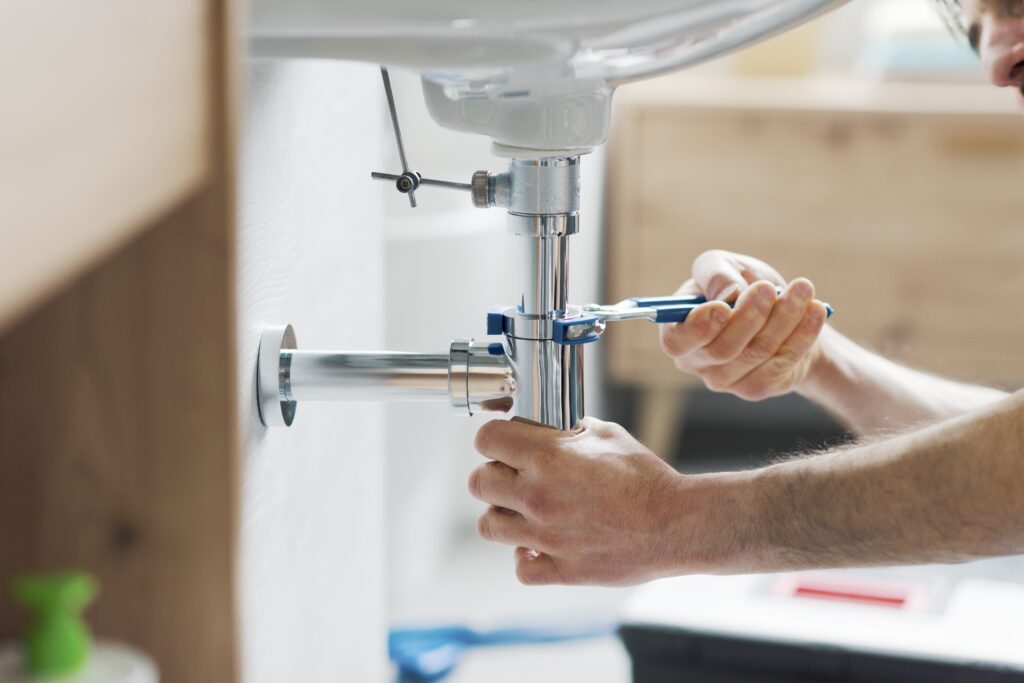 A plumber using a wrench to tighten a bathroom sink pipe, showcasing an essential task for a thorough spring home maintenance inspection.