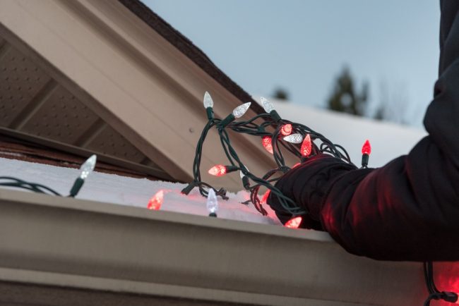 Close up of arms hanging a tangled pile of red and white Christmas lights on a snow covered roof